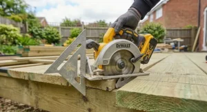 Using a speed square as a straight edge guide for square crosscuts on timber decking with a cordless circular saw.
